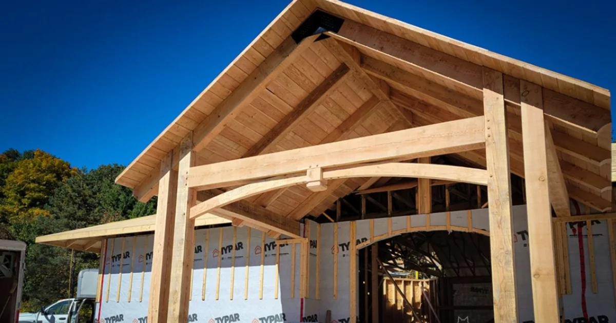 Partially built timber frame entranceway with natural wood beams on a new home under construction.